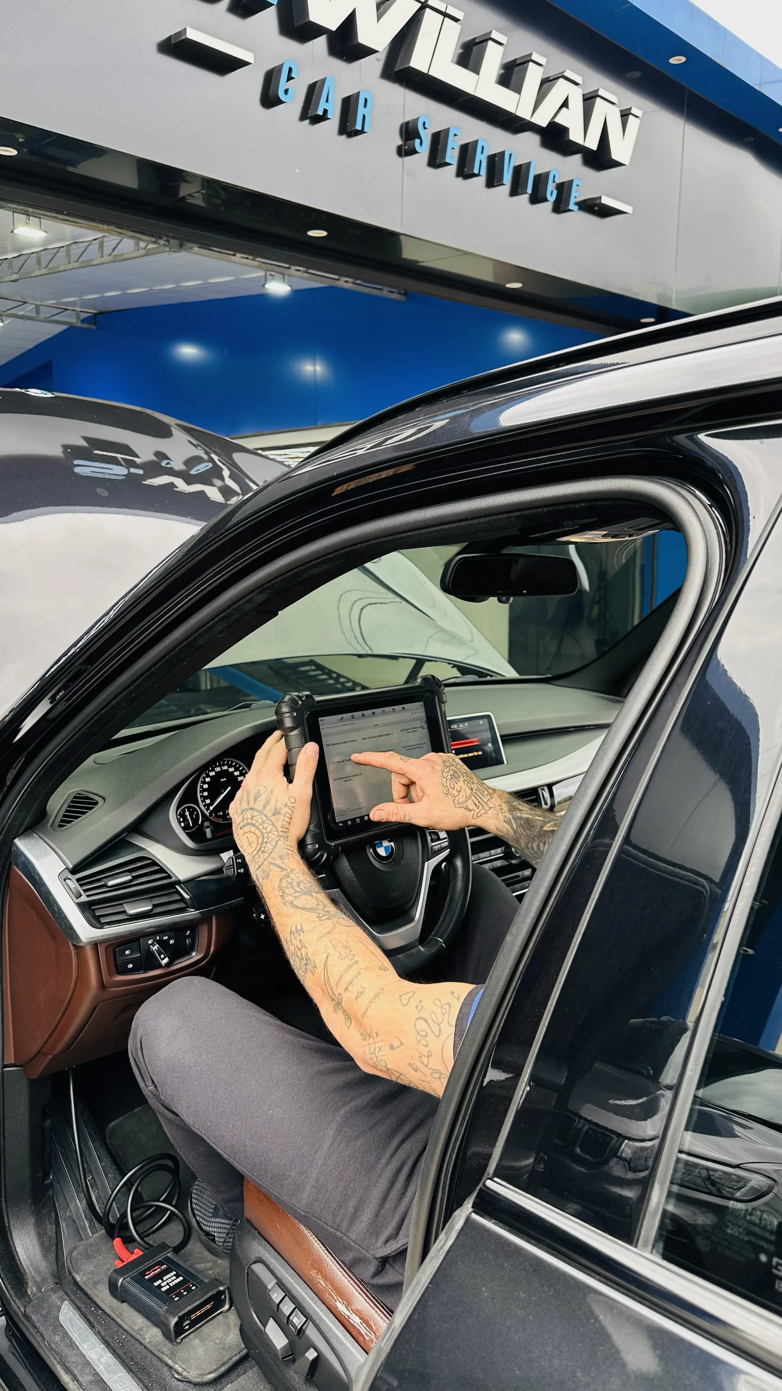 Técnico com um tablet dentro de um BMW, na frente do letreiro da oficina