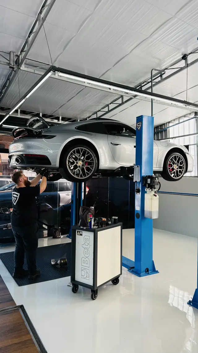Porsche 911 no elevador da oficina, com o técnico trabalhando embaixo